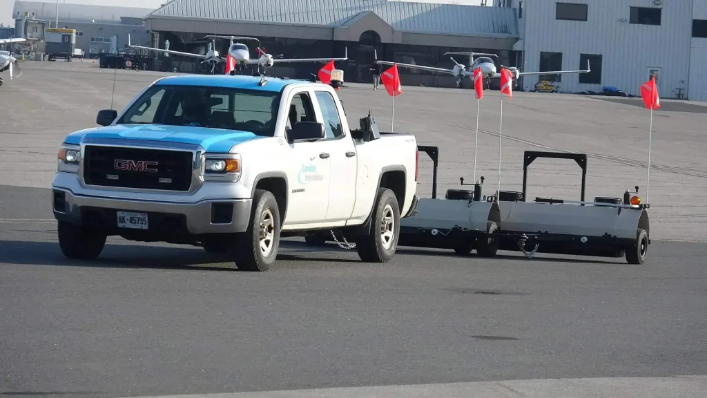 A pickup towing a magnetic bar along the apron area of an airport to collect FOD