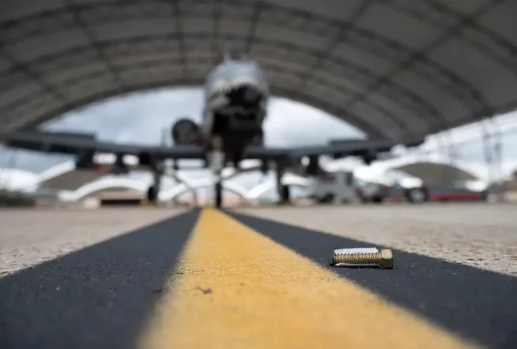 A bolt fallen on the tarmac in front of an aircraft hangar, which is considered foreign object debris.